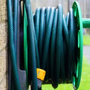 A neatly coiled garden hose on a wall-mounted reel against a brick wall.
