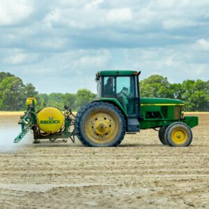 Green tractor with sprayer working in an open farm field under a cloudy sky.